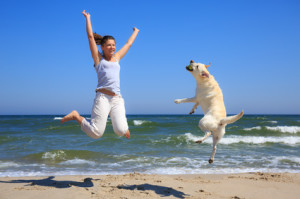 Woman and dog breed Labrador jumping on the beach